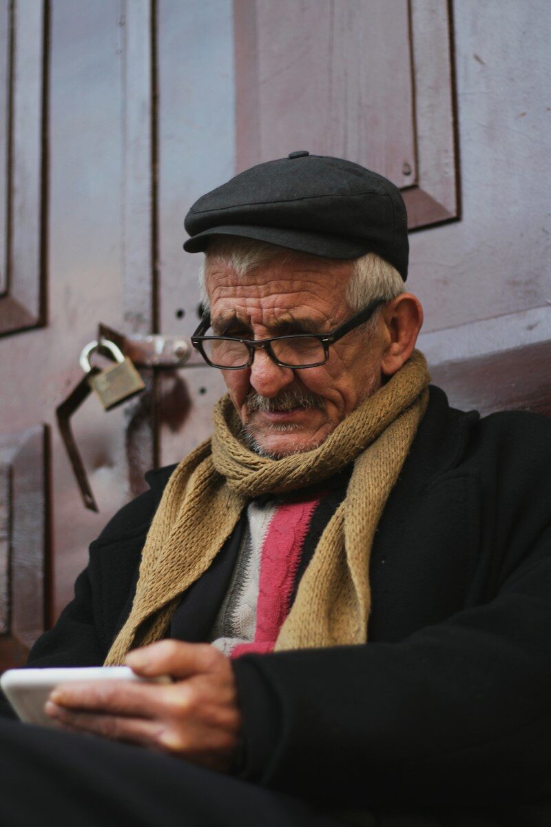 Elderly man wearing glasses and scarf looks at phone